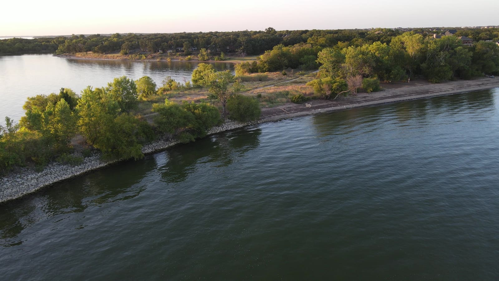 Aerial view of The Cut Trailhead shoreline at golden hour — the tree-lined point and riprap waterline on Lake Lewisville